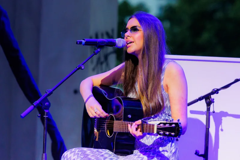 Sirine singing and playing acoustic guitar at the Parieté Gala in Berlin, under blue and violet stage lighting.